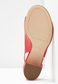 Chaussure femme rouge à dos ouvert vue de la semelle, avec une semelle lisse beige et un petit talon marron texturé sur fond blanc.