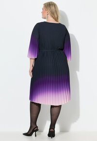 Vestido con pliegues en un degradado de azul marino a púrpura, con mangas tres cuartos y una cintura ceñida con cinturón, combinado con tacones negros.