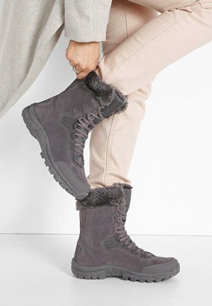 Stivali grigi da esterno con bordo in pelo sintetico, design con lacci, colletto imbottito, suola robusta e tessuto texturizzato, abbinati a pantaloni rosa chiaro.