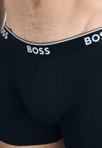 Schwarze Boxershorts aus dehnbarem Stoff, ausgestattet mit einem weichen, elastischen Bund, der das weiße "BOSS"-Logo und goldene Akzentdetails aufweist.