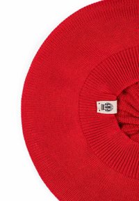 Red knitted hat with a circular shape, featuring a ribbed brim and a textured body. Includes a woven label with a logo.