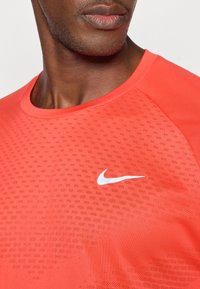 Κόκκινο αθλητικό μπλουζάκι με κοντά μανίκια και υφαντή επιφάνεια, με λευκό λογότυπο Nike στο στήθος. Διαθέτει στρογγυλή λαιμόκοψη και απαλό ύφασμα.