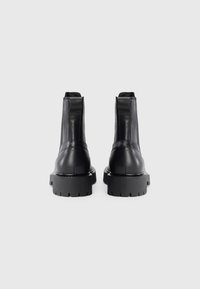 Botas de tobillo de cuero negro con un diseño estructurado, paneles laterales elásticos, suelas de goma gruesas y detalles de hardware mínimos.