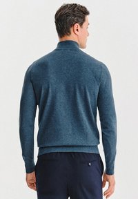 Sweter w ciemnoniebieskim plecionym materiale, z kołnierzem stójkowym oraz ściągaczami przy mankietach i dolnej krawędzi. Zaprojektowany w prostym kroju.