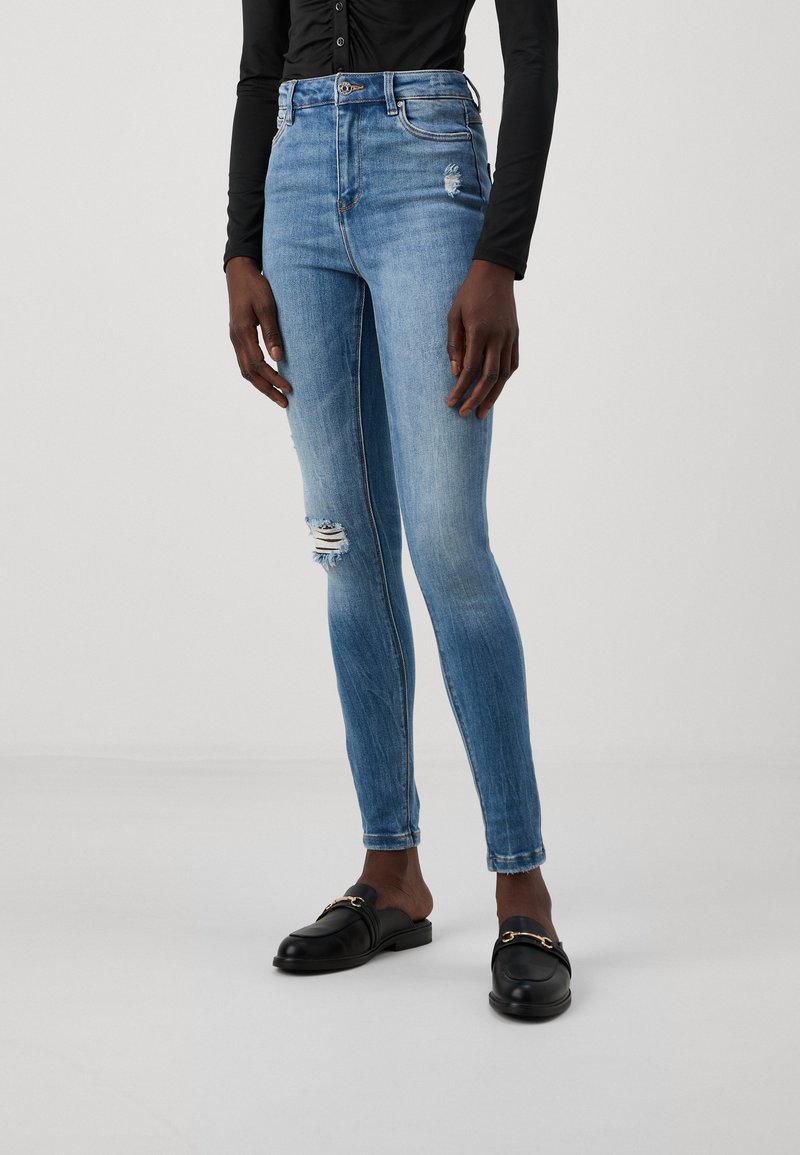 Skinny jeans in light blue denim with a high waist, featuring distressed details and a slight fade. Paired with black loafers.