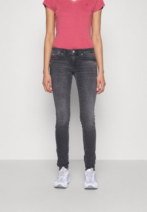Jeans skinny grises con un diseño de cinco bolsillos, combinados con una blusa de manga corta en pico rosa y zapatillas blancas con acentos azules.