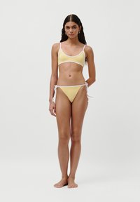 Set de bikini galben cu detalii albe; include un top bralette cu bretele subțiri și un decolteu adânc, asociat cu un fundal legat lateral.