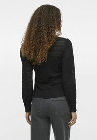 Svart stickad tröja med långa ärmar, texturerad design och puffiga axlar. Kombinerad med mörkgrå jeans som har bakfickor.
