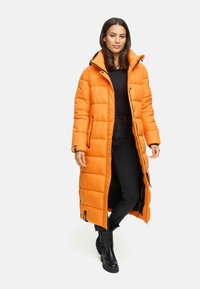 Lange oranje pufferjas met capuchon, voorzien van een gewatteerd ontwerp, ritssluiting en zijzakken, gecombineerd met zwarte jeans en laarzen.