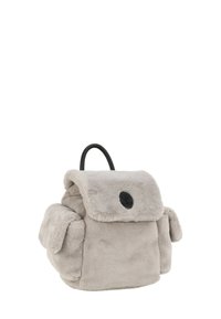 Mochila de felpa gris con solapa, cuerpo redondeado, logo negro y asa corta. Presenta una textura suave y bolsillos laterales.
