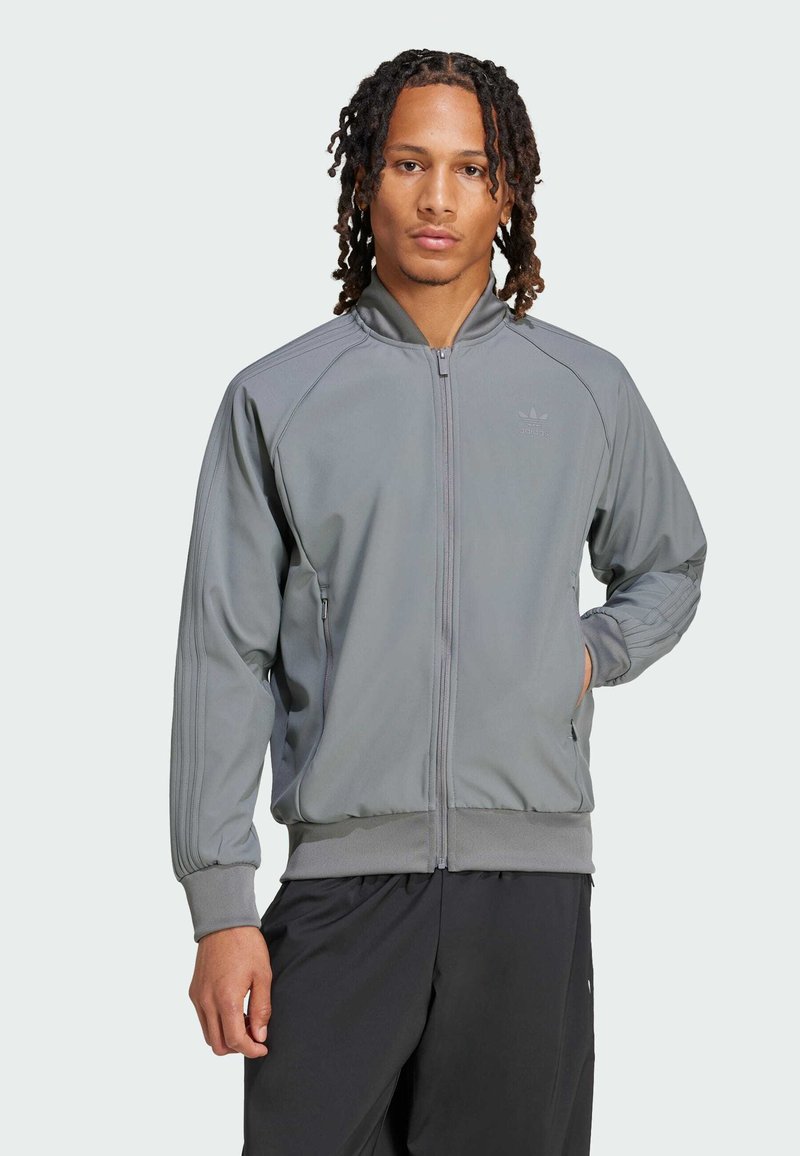 Szara sportowa kurtka z zamkiem z przodu, ściągaczami przy rękawach i u dołu. Posiada boczne paski oraz małe logo na klatce piersiowej. Gładka tekstura materiału.