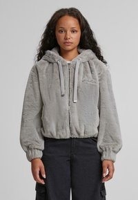 Grå faux fur zip-hoodie med stor hætte, elastiske manchetter og en cropped pasform. Har en lille broderet detalje på fronten.
