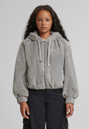 Hallhalli hallhalli kapuutsiga hall kunstkarusnahast jakke, millel on suur kapuuts, elastsed mansetid ja lühike lõige. Esiküljel on väike tikanddetail.