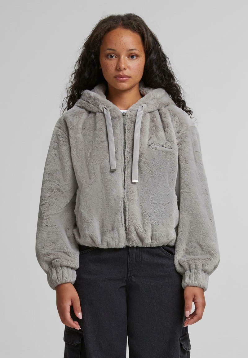 Grå faux fur zip-hoodie med stor hætte, elastiske manchetter og en cropped pasform. Har en lille broderet detalje på fronten.