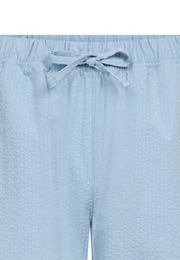 Lichtblauwe pyjamabroek van een gestructureerde stof, met een elastische tailleband en een verstelbaar trekkoord. Er zijn geen zichtbare zakken.
