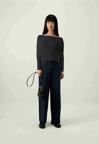 Top preto à mostra dos ombros combinado com calças altas de cintura azul-marinho. Modelo segura uma pequena mala preta; o conjunto possui linhas simples e texturas elegantes.