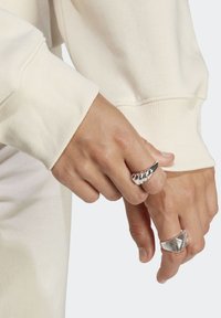 Två silverringar på en hand, en med spiraldesign och den andra med en geometrisk form. Handen vilar mot en ljusfärgad ärm.