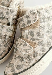 Silberne und beige Leopard-Print-Schuhe mit glitzernder Textur, ausgestattet mit zwei Klettverschlüssen und einer weißen Gummisohle.