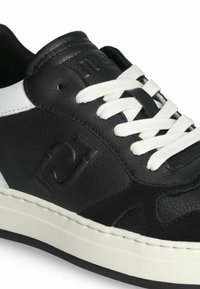 Sneaker in pelle nera con dettagli bianchi, caratterizzato da lacci bianchi piatti, finitura texturizzata e logo in rilievo sul lato. Suola in gomma.