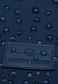 Tessuto navy con texture in rilievo e gocce d'acqua scure. Include un'etichetta in pelle texturizzata con la scritta "JOHNNY URBAN" in rilievo.