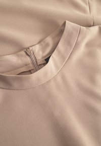 Top bej dintr-un material neted, cu decolteu rotund și un fermoar ascuns la spate. Detalii subtile de cusături și texturi vizibile.