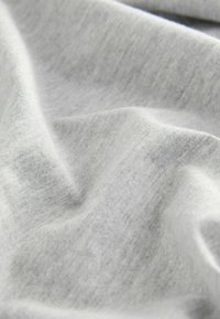 Tissu gris clair avec une texture douce et lisse, présentant des motifs et des plis subtils, indicatifs d'un matériau extensible léger.