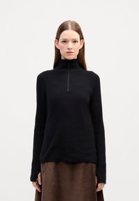 Maglione nero a coste con colletto alto e dettaglio a zip quarti. Presenta maniche lunghe e una vestibilità morbida. Il materiale sembra soffice e texturizzato.