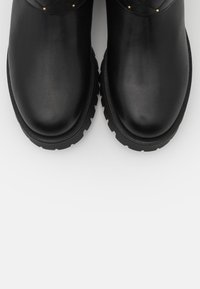 Ein Paar schwarze Lederstiefel mit runden Zehen und dicken, robusten Sohlen auf einem schlichten weißen Hintergrund.