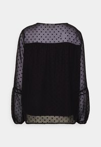 Blouse noire à pois avec tissu transparent, manches longues et détails froncés à l'arrière. Texture lisse avec un design polyvalent.