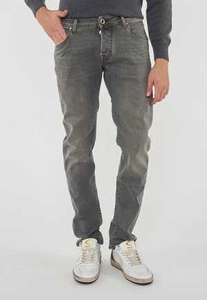 Jeans in denim grigio con leggeri effetti di sbiadimento, design a cinque tasche, bottone e zip argentati, indossati con sneakers bianche con accenti gialli.