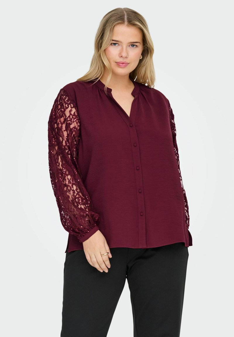 Blusa bordeaux con colletto, bottoni frontali interi e maniche lunghe in pizzo trasparente. Il corpo è in tessuto strutturato, con una vestibilità comoda.