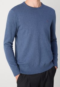 Niebieski sweter dzianinowy z długimi rękawami i okrągłym dekoltem. Posiada ściągacze przy mankietach i w pasie. Małe logo na klatce piersiowej.