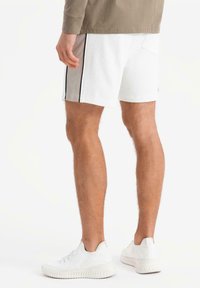 Hvide sport shorts med sorte side-striber, med en baglomme, parret med hvide teksturerede sneakers. Casual pasform.