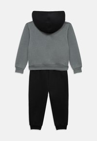 Γκρι φούτερ με μαύρο κουκούλι, συνδυασμένο με μαύρη φόρμα. Διαθέτει ελαστικές μανσέτες και ζώνη μέσης, κατασκευασμένο από μαλακό, υφασμένο ύφασμα.