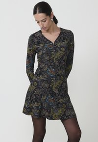 Vestido de manga larga con escote en V, hecho de tela oscura con patrones florales coloridos. Tiene una falda acampanada y un cuerpo ajustado.