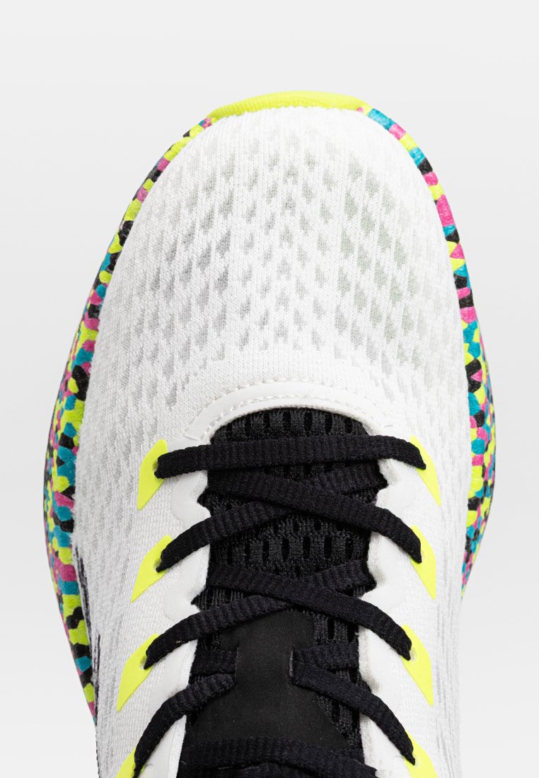 Chaussure de sport avec une tige en mesh blanche, des lacets noirs, des accents jaune fluo et une semelle extérieure colorée à motifs rose, bleu et vert.