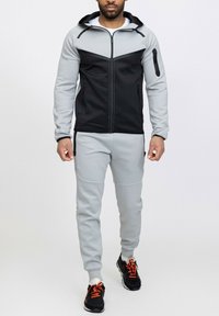 Survêtement à capuche en noir et gris clair ; doté de poches zippées et d'un design ajusté ; fabriqué en tissu texturé et extensible.