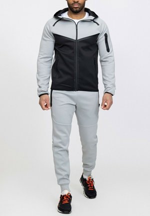 Survêtement à capuche en noir et gris clair ; doté de poches zippées et d'un design ajusté ; fabriqué en tissu texturé et extensible.