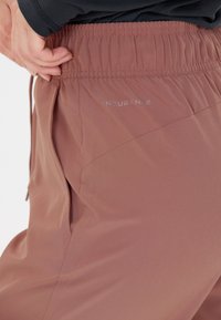 Helle rosa Sporthose mit elastischem Bund, Seitentaschen und einer strukturierten Optik sowie einem dezenten Logo-Detail an der Hüfte.