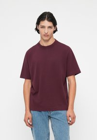 Burgundy lühikeste varrukatega T-särk, millel on lõdvestatud lõige; ümar kaelus ja pehme puuvillane materjal, koos helesiniste teksadega.