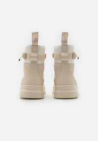 Un paio di stivali alti beige realizzati con un mix di tessuto e pelle, con linguette sul retro e suole in gomma spessa, mostrati vista da dietro.