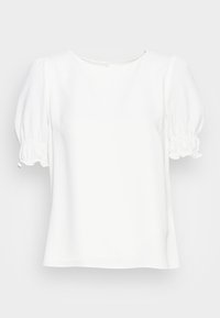 Blouse blanche avec manches courtes bouffantes, poignets à volants élastiqués, et un col rond, présentée sur un fond uni.