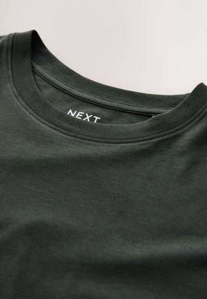 Tumeheline puuvillane T-särk ümar kaelusega, millel on krae valgel tekstil kiri "NEXT". Sile tekstuur, igapäevane disain.
