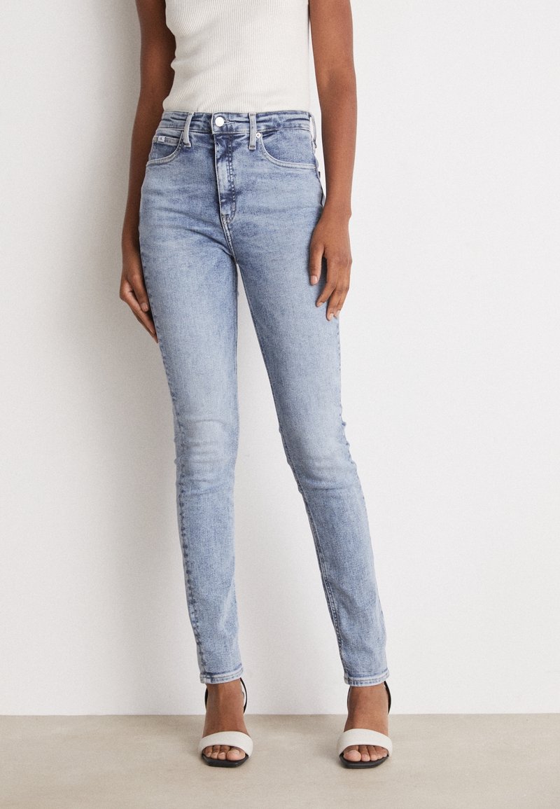 Vaqueros skinny de color azul claro, hechos de denim, con una cinturilla alta, trabillas para cinturón y diseño de cinco bolsillos. Llevados con tacones destalonados.