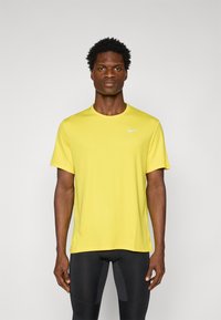 T-shirt jaune Nike à manches courtes avec un col rond et un petit logo blanc sur la poitrine gauche. Le tissu semble léger et lisse.