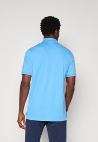 Svetlo modra polo majica s kratkimi rokavi, ovratnikom in stranskimi razporki na robu. Narejena iz gladkega blaga, prikazuje čist, minimalen dizajn.