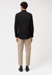 Camicia nera a maniche lunghe con polsini a bottone, abbinata a pantaloni beige a gamba affusolata e stivaletti neri. Tessuto liscio con un design classico del colletto.