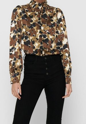 Mujer con blusa floral de manga larga y cuello alto, combinada con pantalones negros de cintura alta con botones frontales.