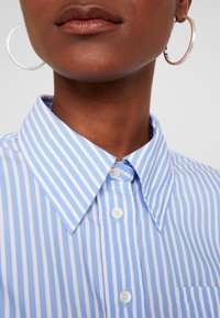Blauw-wit gestreept overhemd met knopen, voorzien van een klassieke kraag en een borstzak. De stof oogt glad en heeft een frisse textuur.