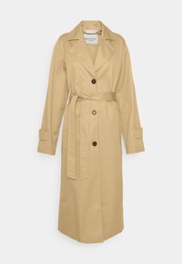 Trench-coat long beige avec larges revers, trois boutons sur le devant, ceinture à la taille et bracelets aux poignets, présenté sur fond blanc.